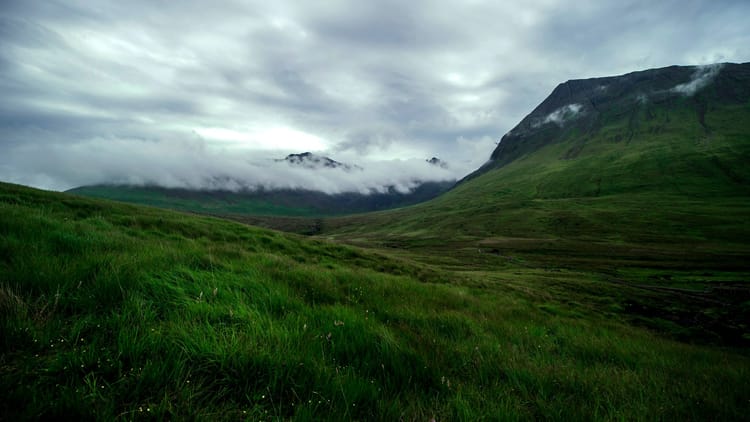 cloud covered mountain in the distance with a grassy valley in the foreground