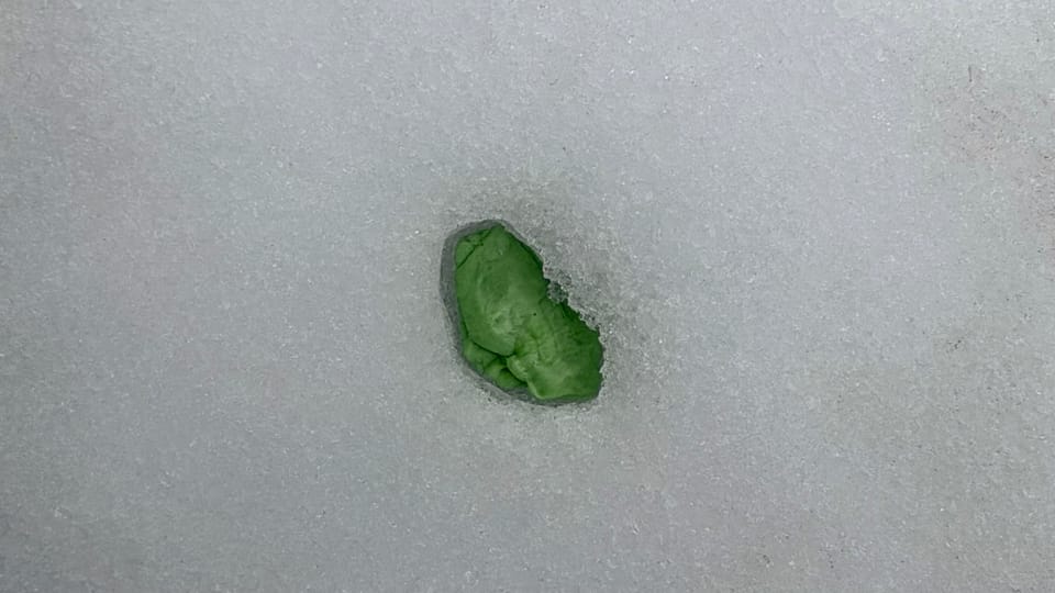 green piece of chewing gum melted down into a surface of icy snow