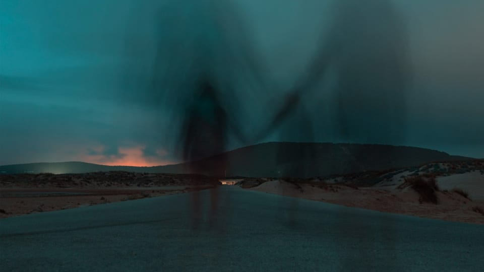 two ghostly figures walking away down a bleak road seemingly holding hands